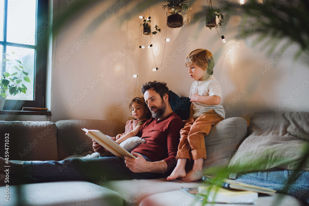 Wall mural Mature father with two small children resting indoors at home, looking at photo album.