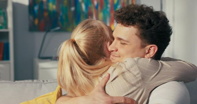 A pretty blonde sits on the couch next to her fianc , hugs him longingly, throws herself on his neck, embraces tightly, expresses pride, satisfaction, praises boyfriend, congratulates