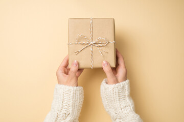 First person top view photo of girl hands in white knitted pullover giving craft paper giftbox with...
