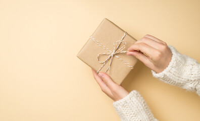 First person top view photo of hands in white sweater unpacking craft paper giftbox with twine bow...