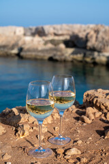 Two glasses of white dry white wine served on rocks in blue sea bay near Protaras touristic town on Cyprus