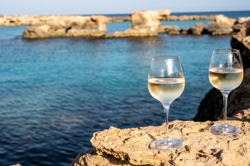 Two glasses of cold white dry white wine served on rocks in blue sea bay near Protaras touristic town on Cyprus