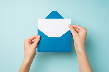 First person top view photo of female hands holding open blue envelope with white paper sheet on isolated pastel blue background with empty space - obrazy, fototapety, plakaty