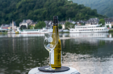 Tasting of white quality riesling wine served on outdoor terrace in Mosel wine region with Mosel river and old German town on background, Germany - obrazy, fototapety, plakaty