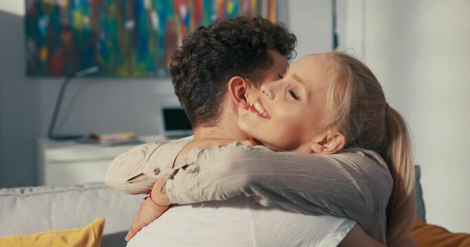 Beautiful blonde sits on the couch next to her fianc , hugs him longingly, throws herself around his neck, embraces tightly, expresses pride, contentment, caring, concern, love