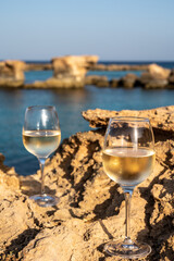 Two glasses of cold white dry white wine served on rocks in blue sea bay near Protaras touristic town on Cyprus
