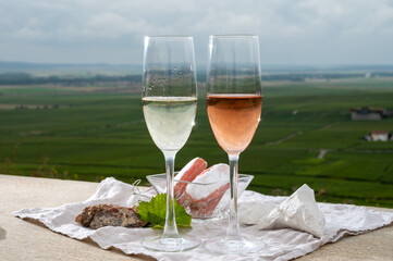 Glasses of white and rose brut champagne wine and examples of vineyard soils, white chalk stones and firestones and view on grand cru vineyards of  Montagne de Reims near Verzenay, Champagne, France