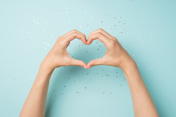 First person top view photo of female hands making heart with fingers on isolated pastel blue...