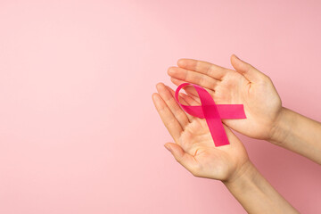 First person top view photo of hands holding pink satin ribbon in palms symbol of breast cancer...