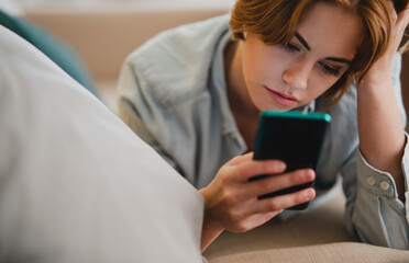 Portrait of young woman using smartphone, lying on sofa at home, social networks concept.