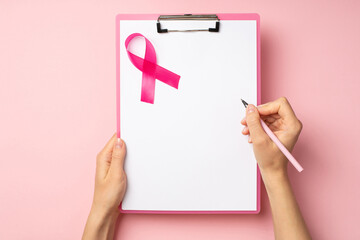 First person top view photo of hands holding pink pen and pink clipboard with paper sheet and pink...