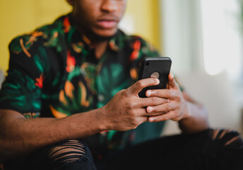 Portrait of unrecognizable young man using smartphone, sitting on sofa at home, social networks concept.