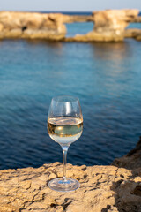 Glass of cold white dry white wine served on rocks in blue sea bay near Protaras touristic town on Cyprus