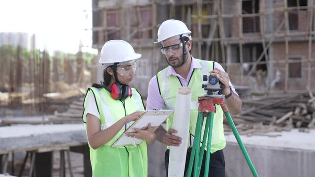 Two Indian man and woman Engineers work at Construction Site with blue prints.Two Asian worker checking work details while using theodolite.civil engineers doing survey on construction site.