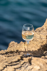 Glass of cold white dry white wine served on rocks in blue sea bay near Protaras touristic town on Cyprus