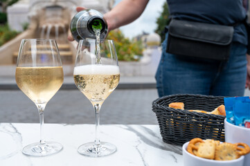 Waiter pouring of brut champagne sparkling wine into glasses in street cafe in old central part of city Reims, Champagne, France