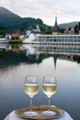 Tasting of white quality riesling wine served on outdoor terrace in Mosel wine region with Mosel river and old German town on background, Germany