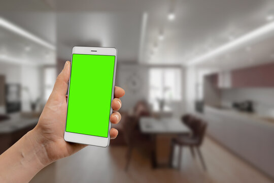 Male hand using smartphone with blank green chroma key screen to control kitchen appliances