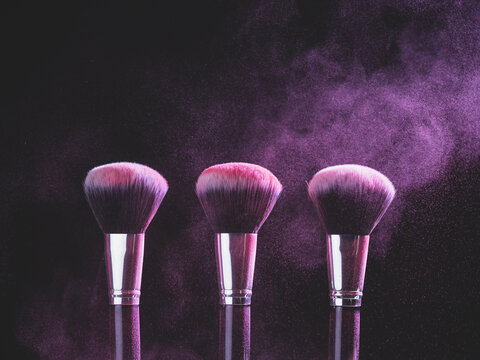 Make-up Brush With Purple Powder Explosion On Black Background