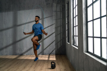 Young African American sportsman using jumping rope indoors, workout training concept.