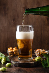 Pouring fresh beer from bottle into beer glass. Brewed and crafted quality product on wooden rustic background. vertical image