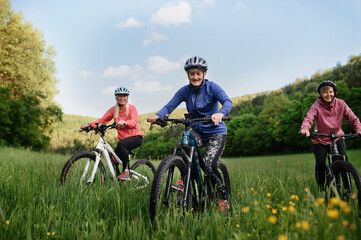 Fototapeta na wymiar Low angle view of happy active senior women friends cycling together outdoors in nature.