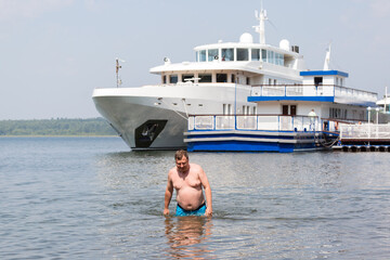 A young oligarch swims in the sea against the background his own yacht.