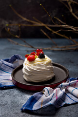 dessert Anna Pavlova on dark blue table with strawberry, red currant and blueberry