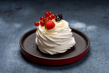 dessert Anna Pavlova on dark blue table with strawberry, red currant and blueberry