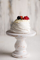 dessert Anna Pavlova with berries on beautiful wooden cake stand on white concrete table, vertical