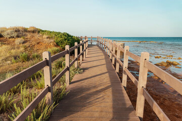 Obraz premium Beautiful peaceful landscape with wooden pier, grass covered hill, calm sea and blue sky