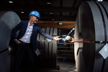 Senior businessman with hardhat taking globe from hand inside metal sheet roll