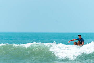 Fototapeta na wymiar Surfer mężczyzna łapiący falę na desce na tle niebieskiego oceanu i błękitnego nieba.