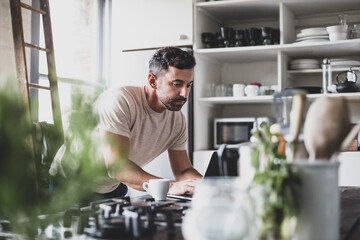 Mid adult hispanic male using laptop in kitchen