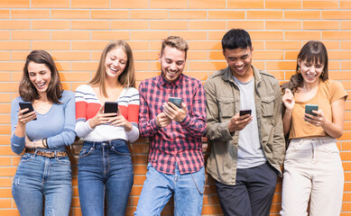 Multicultural friends having fun together looking at their smartphones  at wall on college campus -...