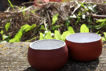 Two handmade brown ceramic cups on a wooden table on green grass background outdoors in the garden