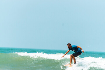 Mężczyzna surfer płynący na fali na tle błękitnego oceanu i nieba. - obrazy, fototapety, plakaty