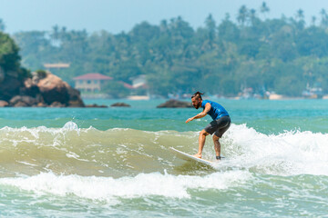 Mężczyzna surfer płynący na fali na tle błękitnego oceanu i nieba. - obrazy, fototapety, plakaty