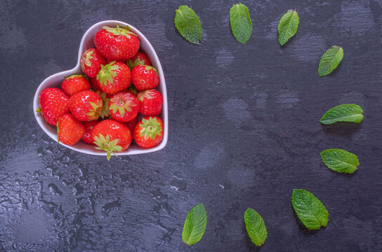 ripe and sweet berry- strawberries in a heart-shaped bowl and mint leaves