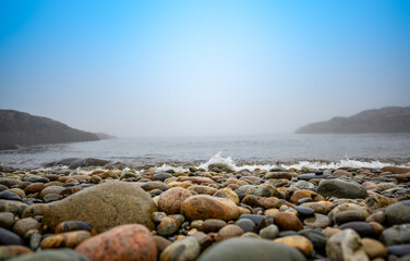Multi-colored round rocks on Little Hunters Beach in Acadia National Park, Maine. Tide coming in as waves crash. 