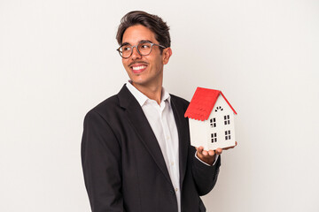 Fototapeta na wymiar Young mixed race business man holding a toy house isolated on white background looks aside smiling, cheerful and pleasant.