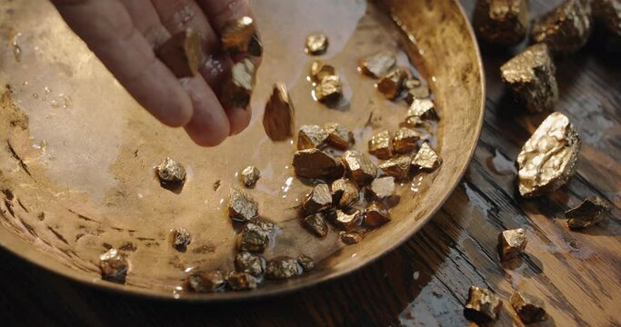 Gold nuggets slowly fall into a copper vintage gold digging bowl. Slow motion 150 fps 4K video. 
