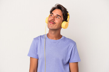 Young mixed race man listening to music isolated on blue background dreaming of achieving goals and...