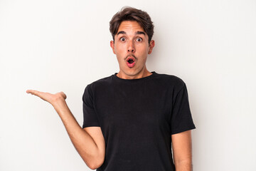 Young mixed race man isolated on white background impressed holding copy space on palm.