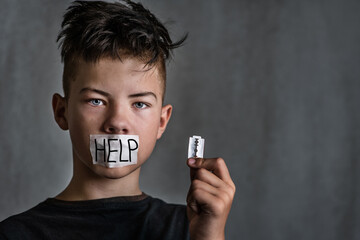 Boy teenager with a mouth sealed with a signature help holding a razor blade in his hand. Growing...