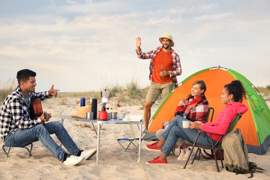 Friends resting near camping tent on sandy beach - Powered by Adobe