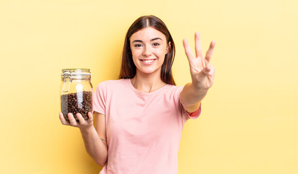 young hispanic woman smiling and looking friendly, showing number three. coffee beans concept
