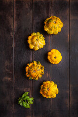 Yellow patissons or squash and a basil leaf on a brown wooden background