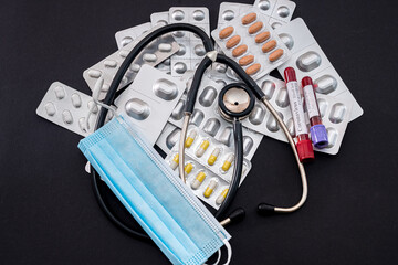 on a beautiful black background lie a stethoscope, a syringe with a sharp needle, and scattered white pills