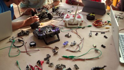 Table top view of multiethnic schoolkids building robots developing program for software robotics engineering using devices at classroom lab. AI technologies development. STEM education concept.